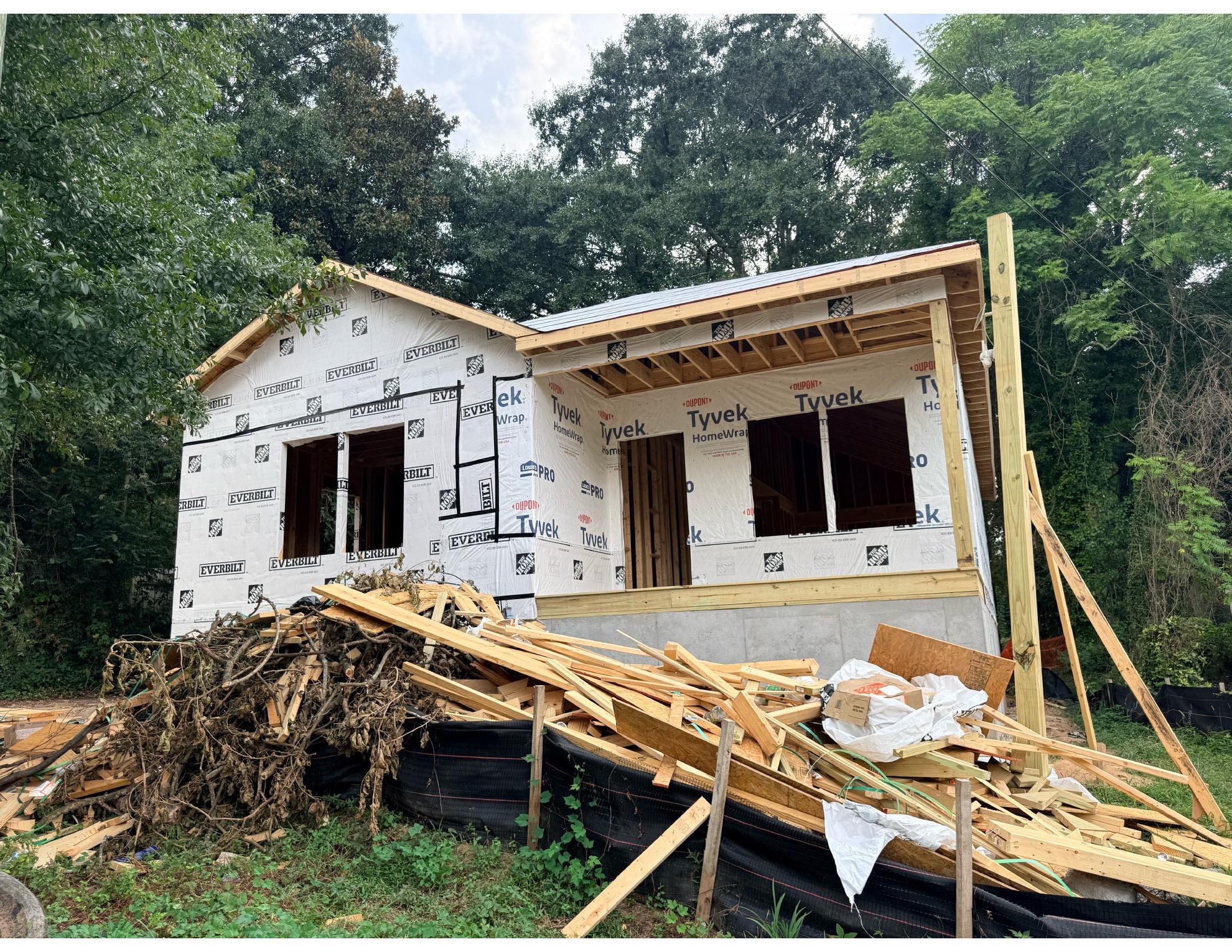 A house under construction with exterior sheathing, new roof framing, and a deep front porch